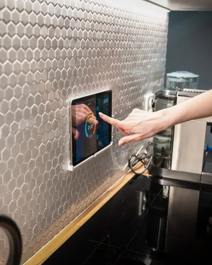 Mano pulsando un panel de control domótico en la pared de una cocina